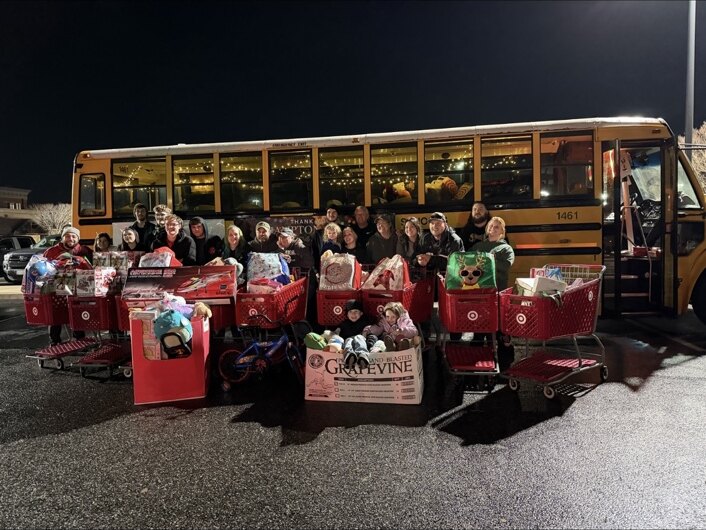 Volunteers with carts of donated toys in front of a school bus